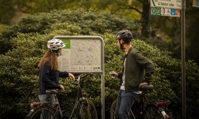 Zwei Radfahrer schauen sich eine Karte im Oldenburger Münsterland an. Durchnummerierte Knotenpunkte zeigen, wo es langgeht. Zwei Radfahrer schauen sich eine Karte im Oldenburger Münsterland an. Durchnummerierte Knotenpunkte zeigen, wo es langgeht.