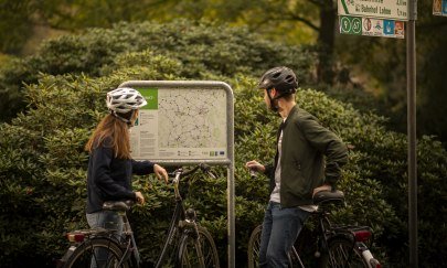 Zwei Radfahrer schauen sich eine Karte im Oldenburger Münsterland an. Durchnummerierte Knotenpunkte zeigen, wo es langgeht. 